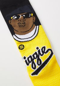 Calcetines de punto con un diseño gráfico de un hombre con un sombrero negro y gafas de sol sobre un fondo amarillo con acentos negros y texto.