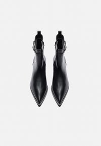 Bottines noires en cuir lisse, avec un bout pointu, une silhouette épurée, une tige courte et des accents à double boucle au niveau de la cheville.