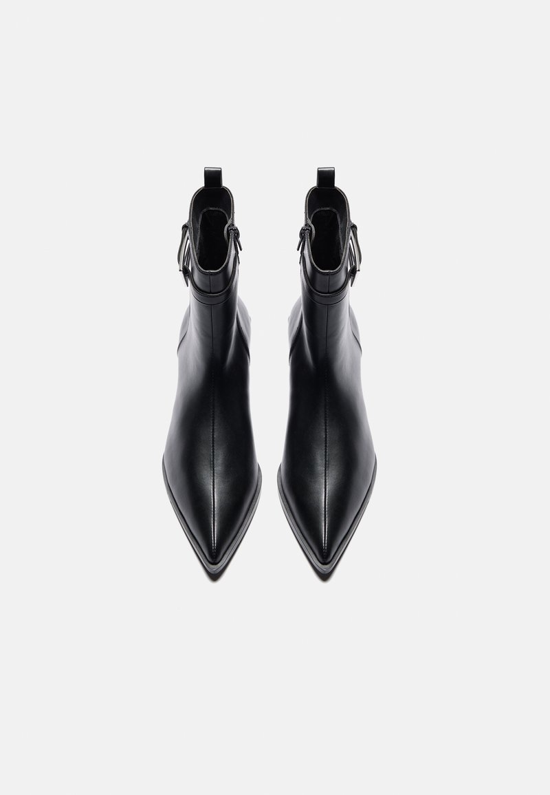 Zwarte enkellaarsjes van glad leer, met een puntige teen, slanke silhouet, korte schacht en dubbele gespsieraden rond de enkel.