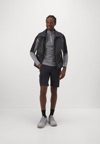 Fleece vest med sorte sider, grå langærmet skjorte, cargo shorts og grå træningssko. Inkluderer lynlåsede lommer og krave.