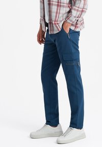 Pantaloni cargo blu in cotone misto, con numerose tasche con cerniera, una vestibilità affusolata e abbinati a sneakers bianche.