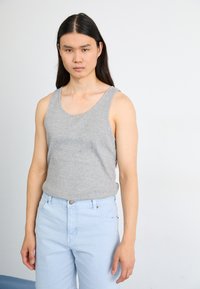 Débardeur gris sans manches en coton, associé à un jean en denim bleu clair avec fermeture par bouton et poches avant.