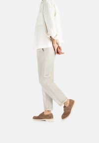 Camicia leggera color crema con taschino, abbinata a pantaloni grigi chiari e scarpe in suede marroni con suole bianche. Sottile trama nei materiali.