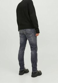 Svart stickad tröja i kombination med mörkblå jeans. Jeansen har en urtvättning och subtila slitningar. Svarta snörstövlar fulländar looken.