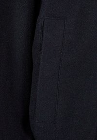 Material întunecat de lână pentru palton, cu o buzunar vertical dreptunghiular cusut pe lateral, evidențiind textura și detaliile cusăturii.