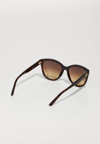 Óculos de sol de padrão tartaruga com lentes castanhas em degradê, formato de olho de gato e detalhes em tons de ouro nas hastes. Armações longas e elegantes.