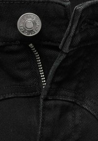Pantalones de mezclilla negros con cierre de botón metálico, cremallera plateada y textura sutil con detalles de costura visibles.