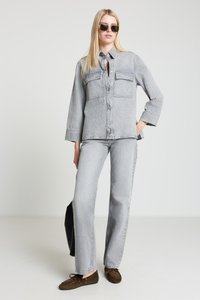 Graues Jeanshemd und passende Jeans, mit durchgehender Knopfleiste, zwei Brusttaschen und geradem Bein. Braune Wildlederschuhe. Klare Sonnenbrille.