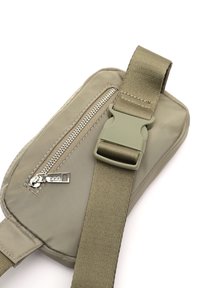 Khaki tkaninová crossbody taška so zipsom, nastaviteľným popruhom a plastovou sponou. Má hladkú textúru a zaoblené okraje.