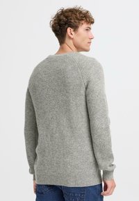 Siv pulover z rebrastim vzorom, dolgimi rokavi, kroj z okroglim izrezom in sproščenim krojem, izdelan iz mehkega pletenega materiala z rahlimi teksturnimi detajli.