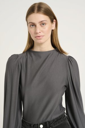 Gray long-sleeve blouse with a smooth texture, featuring puffed shoulders and a high neckline, paired with black high-waisted jeans.