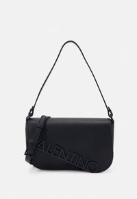 Juodos odos peties rankinė su apvalia forma, priekyje iškilusiais užrašais „VALENTINO“ ir plonu, reguliuojamu dirželiu.