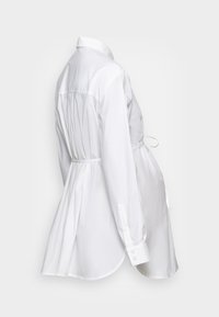 Vit bomullsskjorta med lång silhuett, knäppta manschetter, böjd nederkant och en knutdetalj i midjan för justerbar passform.