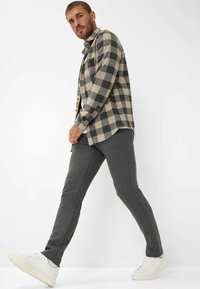 Camicia in flanella a quadri beige e nera, abbinata a pantaloni della tuta grigi e sneakers bianche, con un fit rilassato e classica chiusura a bottoni.