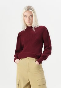 Burgundy ribbed sweater with a high neck and puffed sleeves, paired with beige cargo pants featuring side pockets and a button closure.