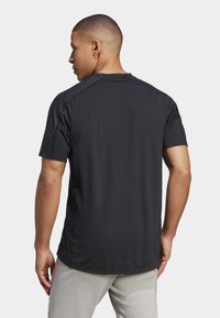 Schwarzes kurzärmeliges Sportshirt mit glatter Textur und Raglanärmeln, das ein dezentes Logo nahe dem Saum aufweist.