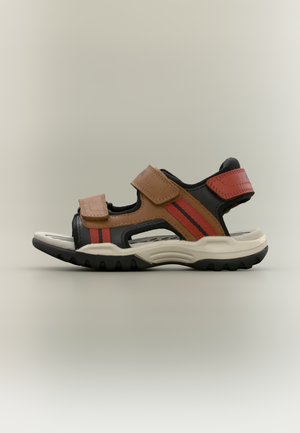 Brun og sort udendørs sandal med røde striber, justerbare stropper, åbent design, tekstureret sål og forstærkede detaljer for holdbarhed.