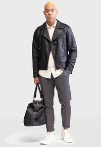 Svart läderbikerjacka, vit knäppt skjorta, grå mönstrade byxor, svart duffelväska och vita högskurna sneakers.
