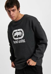 Donkergrijze sweatshirt met een grote witte graphic van een neushoorn en de tekst "*eckö unltd." op de voorkant. Ribgebreide kraag en manchetten.