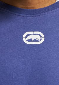 Blue cotton t-shirt featuring a white logo of a rhinoceros within an oval, positioned on the chest area, with a crew neck design.