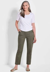 Weißes Kurzarm-T-Shirt kombiniert mit olivgrünen geraden Hosen mit Vorderstaschen und sichtbaren Nähten. Hellfarbene Sandalen.