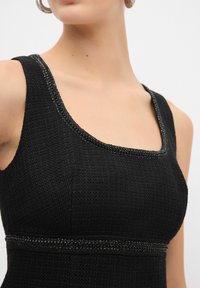 Abito nero in tessuto texturizzato con scollatura quadrata e bordo decorato con perline. Le cuciture dettagliate lungo la vita valorizzano il design.