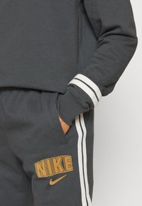 Dark gray Nike sweatshirt and sweatpants with white stripes. Sweatpants have a gold "NIKE" logo and a small gold swoosh on the side.