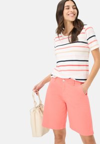 Gestreept t-shirt met korte mouwen in wit, roze en navy; koraalkleurige shorts; model houdt een lichtbeige tas vast, toont casual zomerkleding.