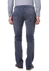 Mężczyzna w wyblakłych ciemnoniebieskich dżinsach i jasnoniebieskiej koszuli w kratę, stojący z rękami swobodnie wzdłuż ciała na białym tle.