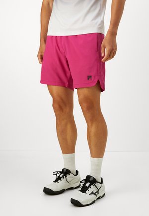 Man wearing bright pink athletic shorts, white crew socks, and white and black sports shoes standing against a plain white background.