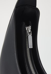Black leather handbag interior with a silver zipper, featuring a branded zipper pull. Textured surface, simple design, and curved shape.