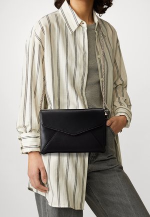Sort læderkuvertpose i stil med en envelope med en kædetræksrem, der har et minimalistisk design og glat tekstur. Båret over en stribet skjorte.