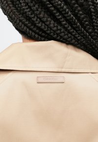 Χακί, ελαφρύ μπουφάν με γιακά που διπλώνει και ετικέτα λογότυπου Calvin Klein σε μινιμαλιστικό σχεδιασμό. Διαθέτει λεία υφή υφάσματος.