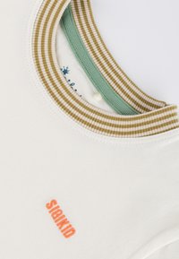 Weißes Baumwoll-T-Shirt mit einem Kragen, der olivfarbene und cremefarbene Streifen hat. Enthält eine kleine orangefarbene "SIGIKID"-Bestickung auf der Vorderseite. Weiche Textur.