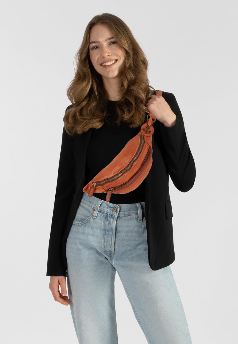 Orangefarbenes Leder-Crossbody-Bag mit zwei Reißverschlussfächern, strukturierter Oberfläche, lässig über der Schulter getragen. Verfügt über einen runden Hardware-Akzent.