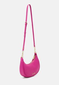 Sac d'épaule rose vif en forme de croissant avec bandoulière réglable et fermeture éclair dorée, avec petit logo doré "Steve Madden" sur le devant.