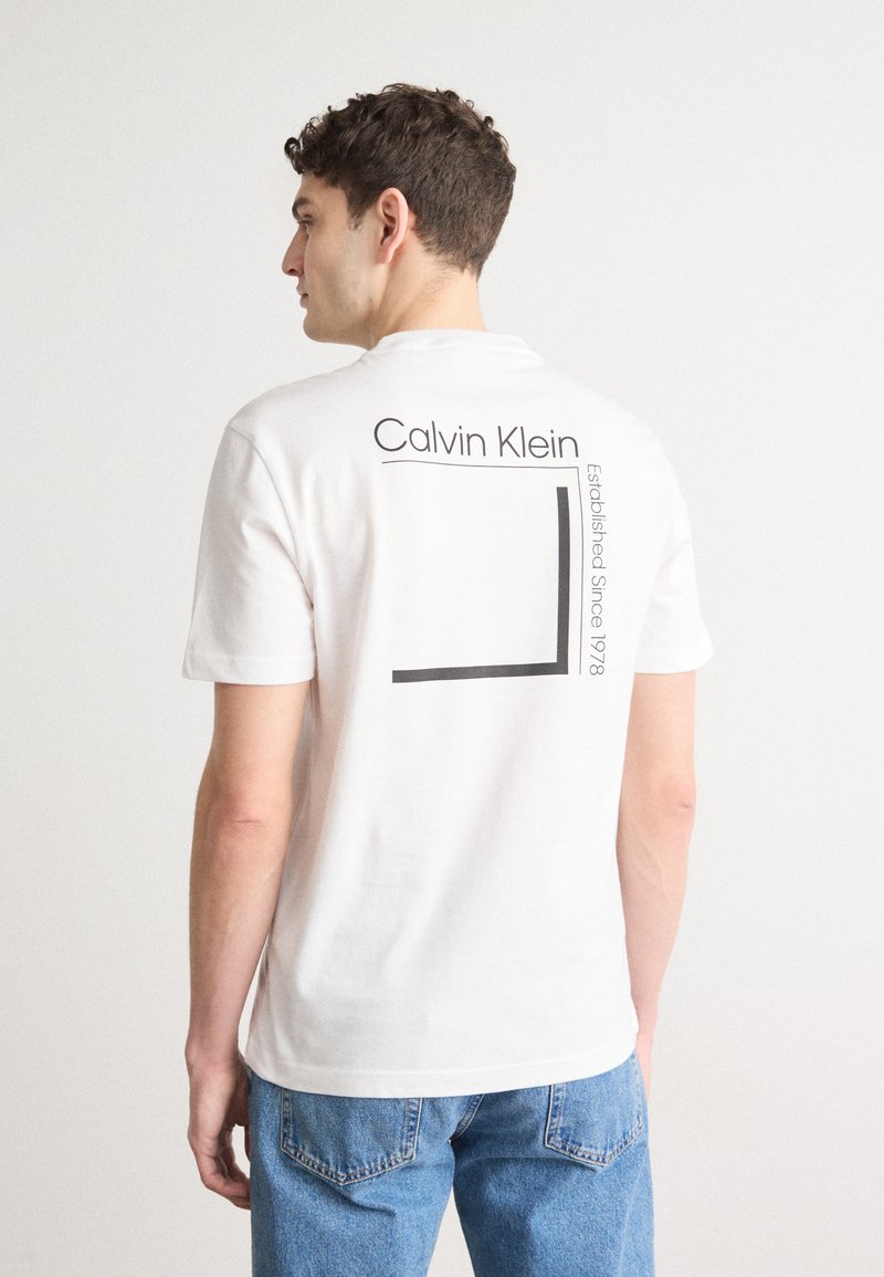 Hvid bomulds t-shirt med sort "Calvin Klein" tekst og et rektangulært grafik på ryggen. Korte ærmer og en afslappet pasform.