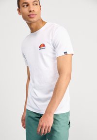 Weißes Baumwoll-T-Shirt mit einem rot-orangen halbkreisförmigen Logo auf der Brust, kurzen Ärmeln und einem marineblauen Akzent am Ärmel.