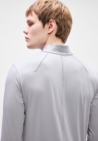 Ανοιχτό γκρι πουκάμισο μακρυμάνικο με υφή, με ψηλό γιακά και διακριτές ραφές στην πλάτη.