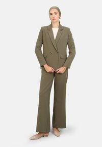 Blazer olive vert à double boutonnage associé à un pantalon large assorti ; présente des lignes épurées et un léger lustre, complété par un haut crème.