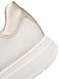 Primo piano del tallone di una sneaker in pelle beige con collo in metallo dorato e suola spessa in gomma bianca.