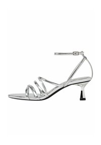 Sandale argentée à fines lanières en matériau métallique, avec un petit talon et une bride autour de la cheville, présentant une texture lisse et brillante ainsi qu'un design minimaliste.