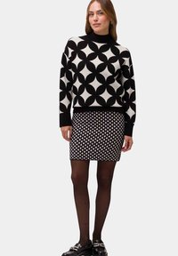 Black and white patterned sweater with geometric designs paired with a black and white skirt featuring diamond patterns, worn with black tights.