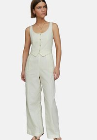 Jumpsuit en lin beige clair avec un corsage ajusté, un col rond et cinq boutons. Il présente des jambes larges et un tissu texturé.