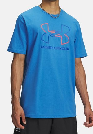 Mand iført en knaldblå Under Armour t-shirt med stort logo og tekst, kombineret med sorte shorts og en sølvkæde halskæde.