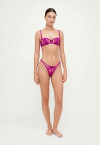 Conjunto de lingerie em renda fúcsia vibrante, apresentando um sutiã balconette com alças ajustáveis e um fio dental a condizer, ambos com delicados detalhes em laço.