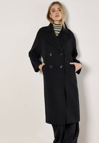 Schwarzer doppelt-knöpfiger Mantel mit großen Knöpfen, breiten Revers und seitlichen Taschen. Verfügt über eine strukturierte Silhouette und eine weiche Textur.