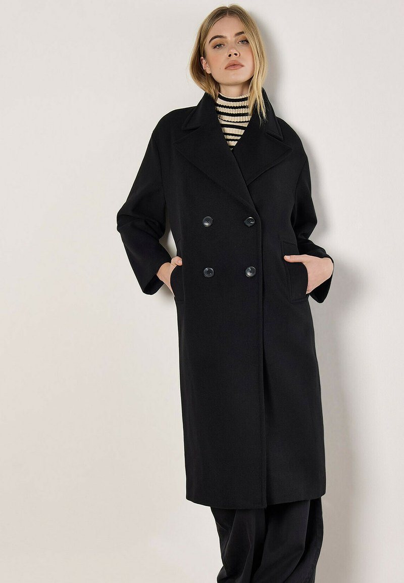 Schwarzer doppelt-knöpfiger Mantel mit großen Knöpfen, breiten Revers und seitlichen Taschen. Verfügt über eine strukturierte Silhouette und eine weiche Textur.