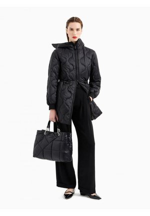 Giacca puffer nera trapuntata con cappuccio e vita regolabile, abbinata a una borsa a spalla nera trapuntata e pantaloni neri a gamba larga.