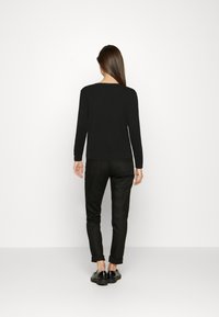 Schwarzes langärmliges Oberteil, taillierte Passform, weicher Stoff, Rundhalsausschnitt, kombiniert mit schwarzen Hosen mit umgeschlagenen Säumen und glänzenden schwarzen Schuhen.